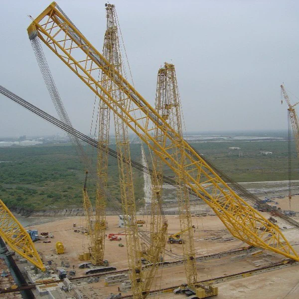 A landscape view of a construction site featuring multiple large yellow cranes, including the notable HLD, surrounded by open land and a body of water.
