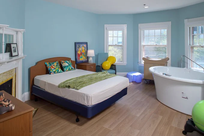 A pale blue room with a birthing tub, a double bed, and birthing equipment