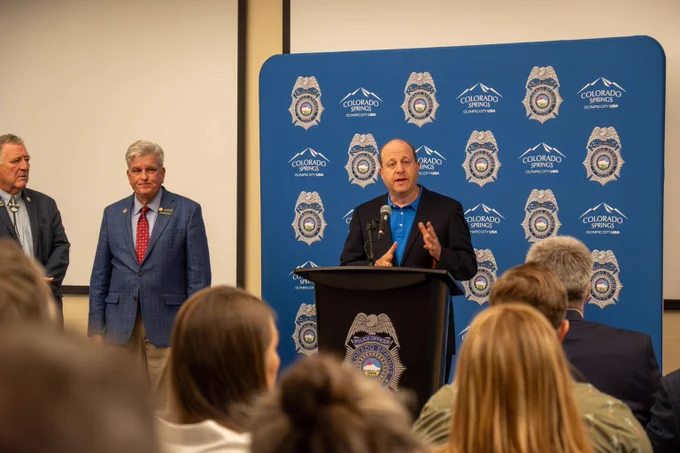 Governor Jared Polis speaks to an audience from a podium with a Colorado Springs Police backdrop during a Bill Signing.