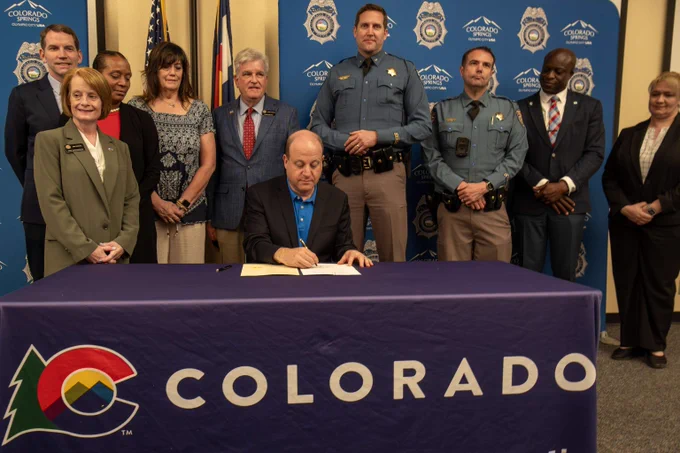 Group of officials and community members gathered around a table with Colorado Governor Jared Polis signing a bill.