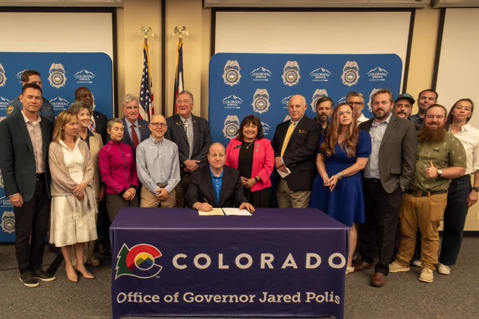 Group of officials and community members gathered around a table with Colorado Governor Jared Polis signing a bill.