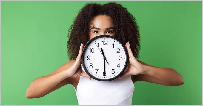 A woman is holding a clock showing the time as 11:30 a.m. The clock obscures her face.