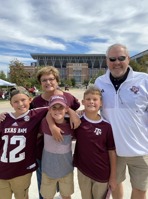 A group of individuals dressed in Texas A&M clothing pose in front of Kyle Field on a sunny day.