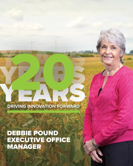 A Debbie Pound stands in a field with tall plants, wearing a pink sweater. The image features large text reading "20 Years Driving Innovation Forward" and mentions "Debbie Pound Executive Office Manager." The sky is partly cloudy. ProAg is an equal opportunity provider and employer.