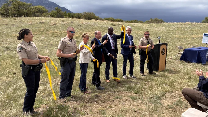 Cheyenne Mountain State Park Officers Jasmine Wolcott, left, and Mike Ivis, far right, hold a ceremonial ribbon as special guests, from right, Jim Petterson, Colorado and Southwest Director; Colorado Springs Mayor Yemi Mobolade; Colorado Governor Jared Polis; Colorado Parks and Wildlife Director Laura Clellan, and Park Manager Jason Hagan make the ceremonial cut, officially expanding the park to 3,187 acres. The day also included signing of a lease between Colorado Parks and Wildlife and Colorado Springs Utilities to establish recreation including camping and watercraft recreation (hand launched/hand-powered) on Rosemont Reservoir. (CPW Photo/Dean Miller)