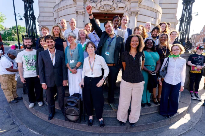 Lambeth's Green councillors standing on the steps of Lambeth Town Hall with big smiles and rainbow lanyards 