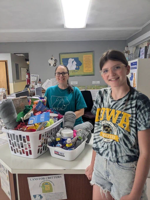 Jenna Puttmann and PAWS & More staff smiling with a laundry basket full of pet toys and supplies and another white tub of pet supplies