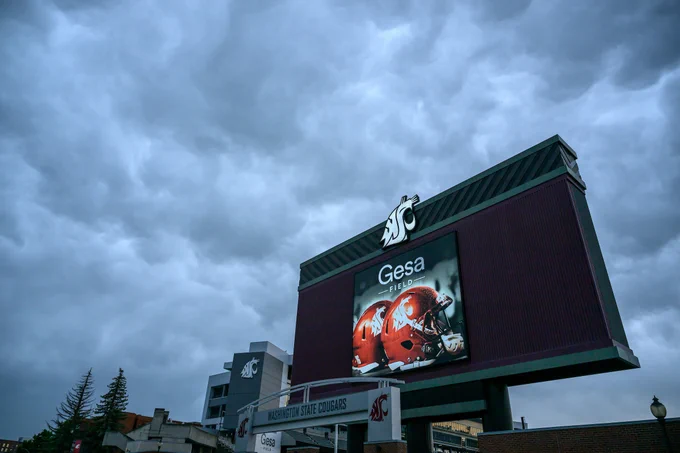 Dark gray clouds sit above a large red structure with a large white W S U spirit head logo and the words Gesa Field below. 