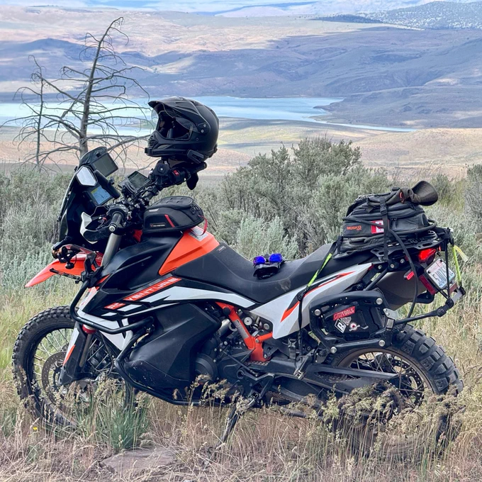 Adventure KTM motorcycle in the wilderness with a lake in the distance, parked with a helmet and miscellaneous items on the back.
