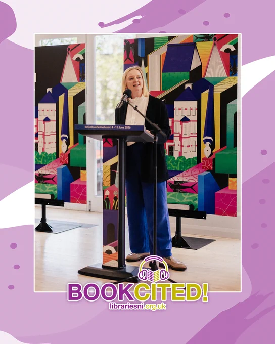 A woman speaks at a podium during the Belfast Book Festival, with a colourful abstract mural behind her.