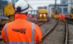 A person wearing a Network Rail jacket and helmet is looking outwards towards railway tracks, where engineering work is taking place 