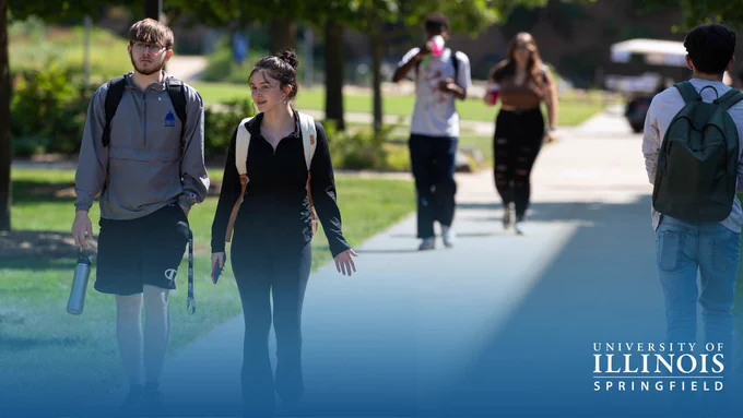 Students walk along a campus path on a sunny day. University of Illinois Springfield logo in bottom right corner.