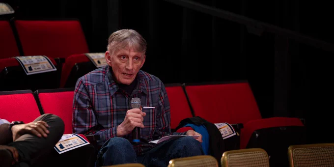 A person is seated alone in a red chair with a hand resting on their chin. 