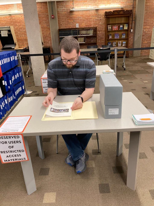 Person seated at a library table reviewing archival documents labeled as restricted access materials.