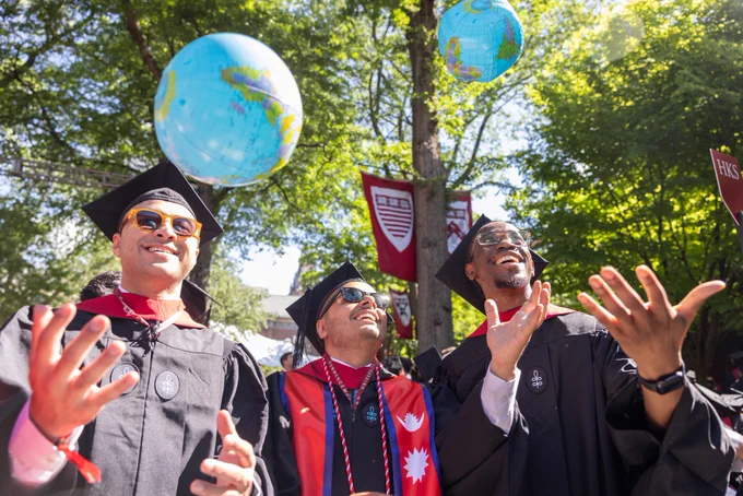 Three graduates in sunlight throwing inflatable globes in the air.