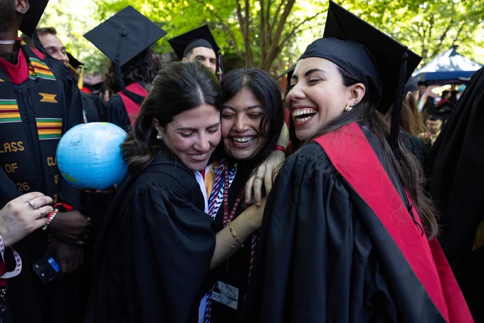Three graduates hugging and smiling in a crowd.