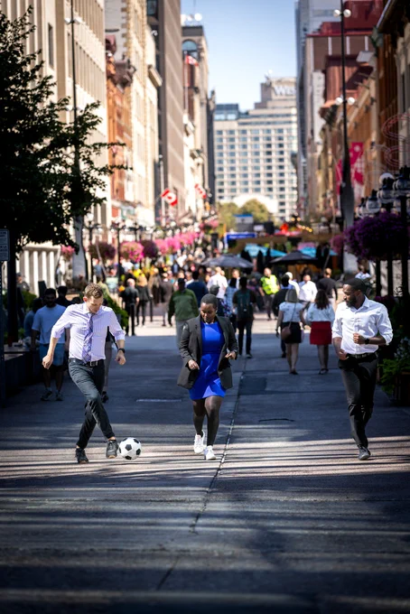 Three people passing a soccer ball in a downtown city of Canada