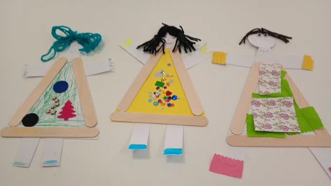 Three colourful paper dolls made from popsicle sticks, showcasing different outfits and hairstyles for imaginative play.