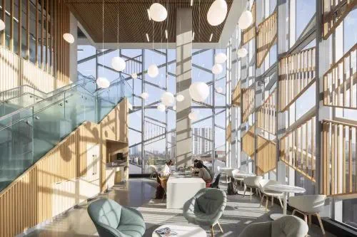 Spacious modern interior with high ceilings, large windows, and hanging pendant lights. Two people sit at a central table. Bright, airy atmosphere.