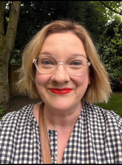 It’s me. In our garden. Generic greenery in the background. Me in the foreground in a checked black and white dress (cub and pudding) with short blonde hair and red lipstick. Smiling. Fucking cake day isn’t it.