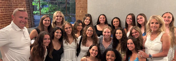 President Daly with Coach Sullivan and Fallon and Softball team smiling for photo at dinner