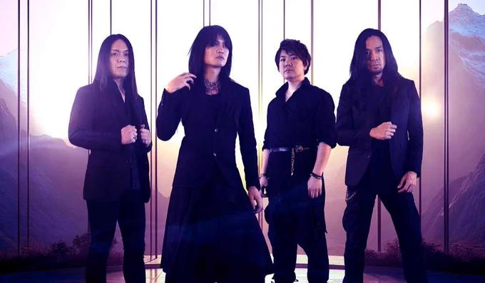 Photo of the four-piece alternative metal band Esprit D'Air standing side by side on a location with a mountain range on the background. All the members are dressed in black clothing, with gothic and metal elements.