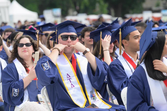 A graduate whistles loudly while seated.