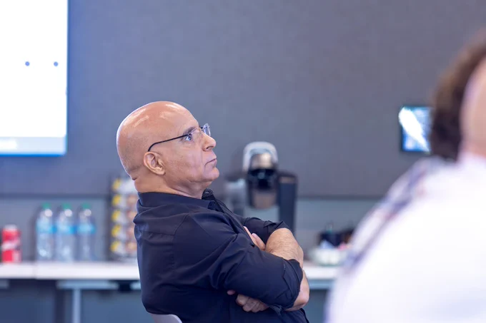 A man sits in a large, modern lecture hall and listens as a fellow scientist gives a presentation on his research.