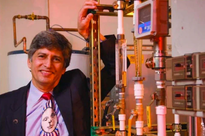 Man in a suit posing with piping and lab equipment in a mechanical room.
