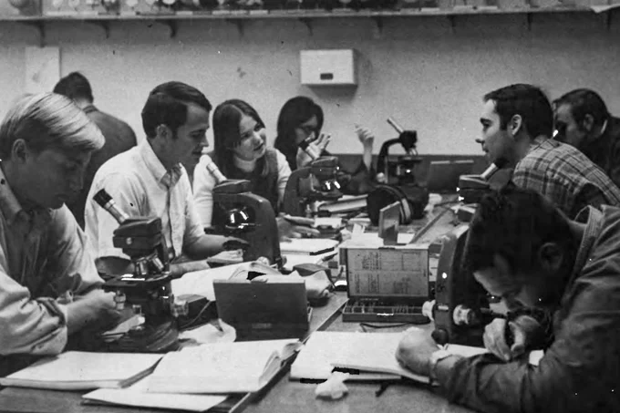 Group of students in a classroom using microscopes and taking notes.