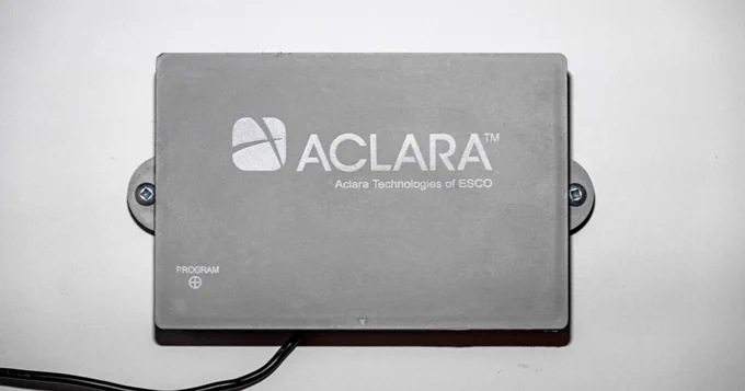 Rectangular gray device labeled 'ACLARA' with 'Aclara Technologies of ESCO' printed on top, mounted on a white surface with screws on each side.