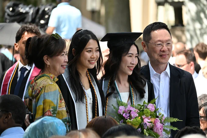 Two MIT graduates stand with their family members for a photo on Killian Court.