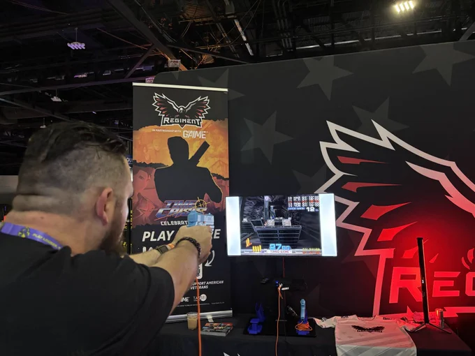 A person interacts with a gaming setup at a convention booth, featuring promotional materials and a video game display.