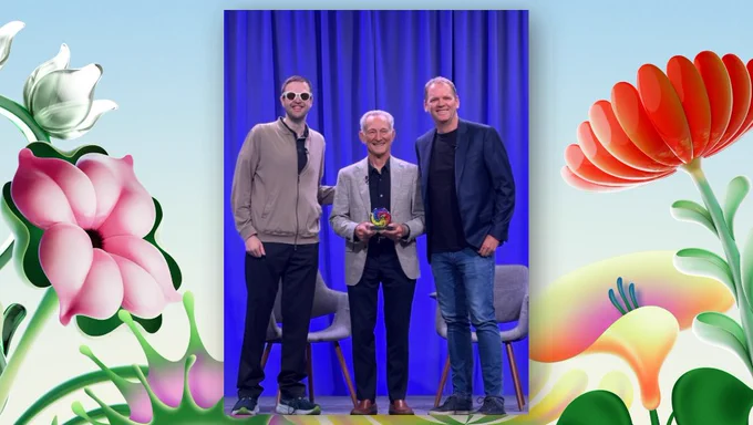 Three people stand on a stage in front of a blue curtain, with two gray chairs behind them. Murray Sargent stands in the middle holding a small, colorful award as it is presented to him, with one person on each side. The photo was taken on May 18, 2026 during the award presentation.