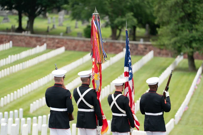 Photo of four UMA members with flags standing in front of the National Cemetery in Alexandria, VA.