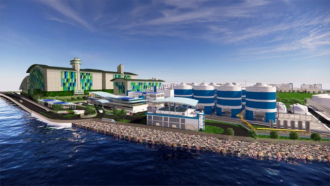 Modern industrial facility with large blue and white storage tanks beside a waterfront under a partly cloudy sky.