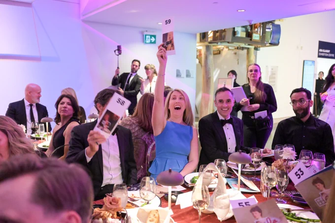 Maybe people seated. In the middle, a woman with a blue top is holding up an auction number.