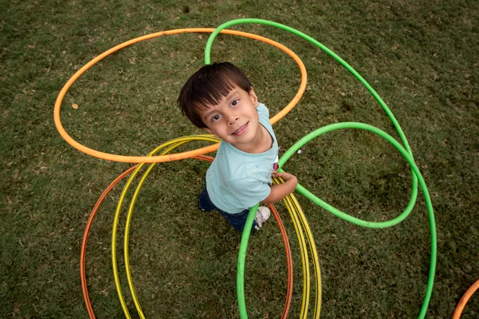 A boy surrounded by colorful hula hoops looks up and smiles at the camera.