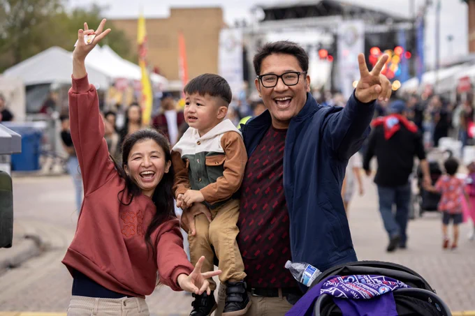 A smiling family of 3 gives the peace sign and smiles for the camera.