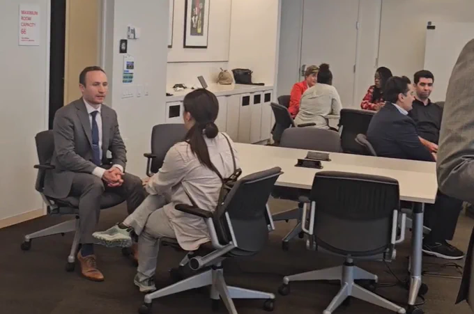 Professionals engaged in small group discussions around tables in a modern office meeting room.