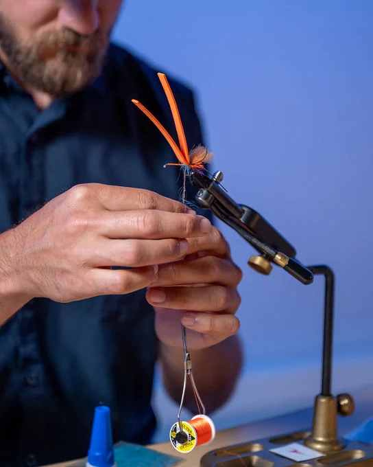 Fly fisherman tying an orange and blue fly for luring in fish. 