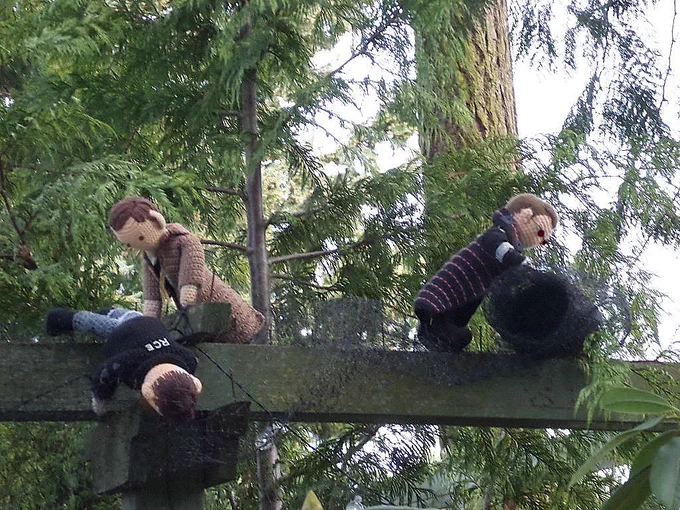 Crochet dolls of Marshal Kahler & Adolphus Murtry maneuvering the deer net over a set of arbor crosspieces while Vinsher Grath pushes the roll further along the arbor planks. Foliage in the background. 
