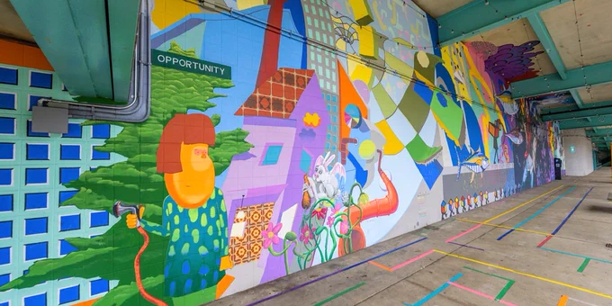 Colorful mural under a bridge, featuring abstract shapes, buildings, and whimsical characters. A sign reads "Opportunity," conveying optimism.