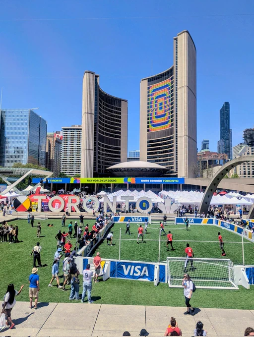View of Nathan Philips Square from the south. A soccer game is happening in the foreground and newcomer day Fair is in the background 