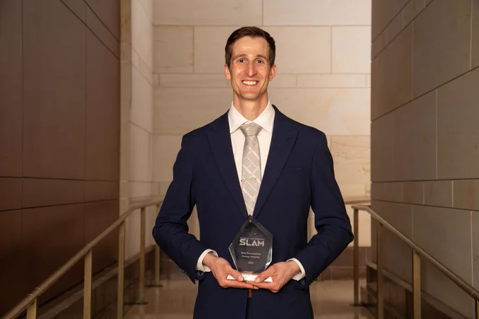 A person in a suit and tie holding an award and smiling at the camera