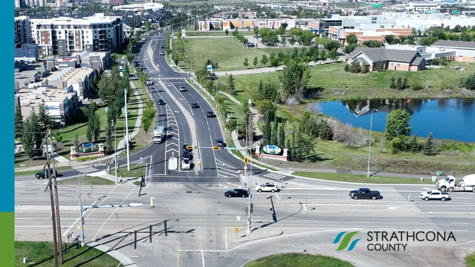 Aerial view of a busy intersection with multiple lanes, surrounded by residential buildings, green spaces, and a pond in Strathcona.