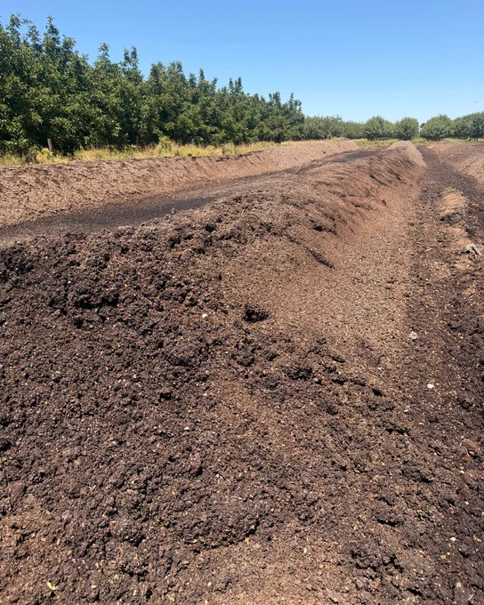 Fresh compost stretched across a farm field under a clear blue sky with green trees lining the horizon.