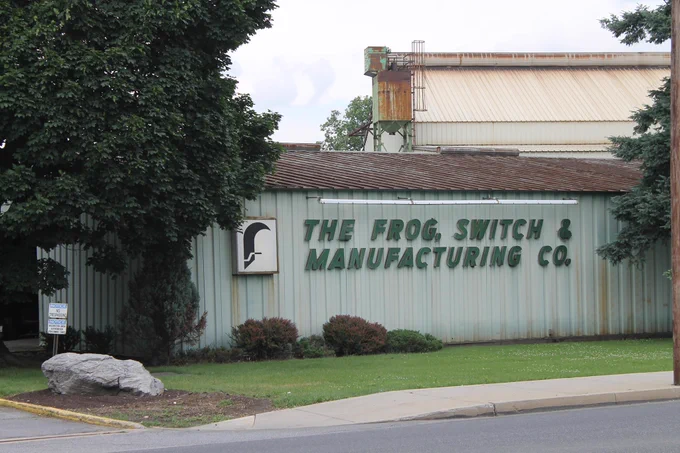 Exterior view of former The Frog Switch & Manufacturing Co. building with green metal siding and surrounding trees.