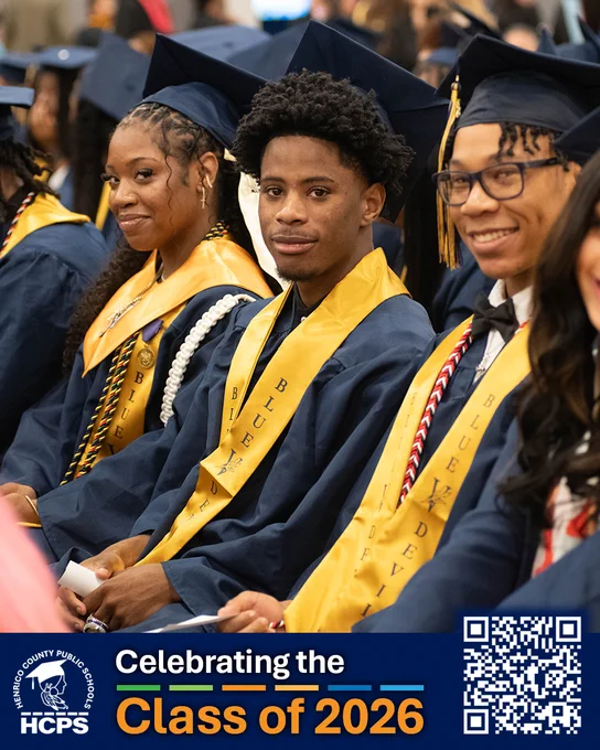 Graduates in navy gowns and yellow sashes at a graduation ceremony, "Celebrating the Class of 2026" banner visible.