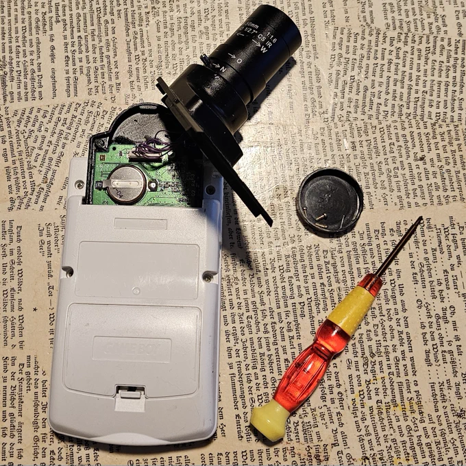 Die Rückseite eines weißen Game Boy Color. Es ist die untere Hälfte eines Game Boy Kamera Cartridges eingesetzt, die obere Hälfte samt Objektiv nicht. 